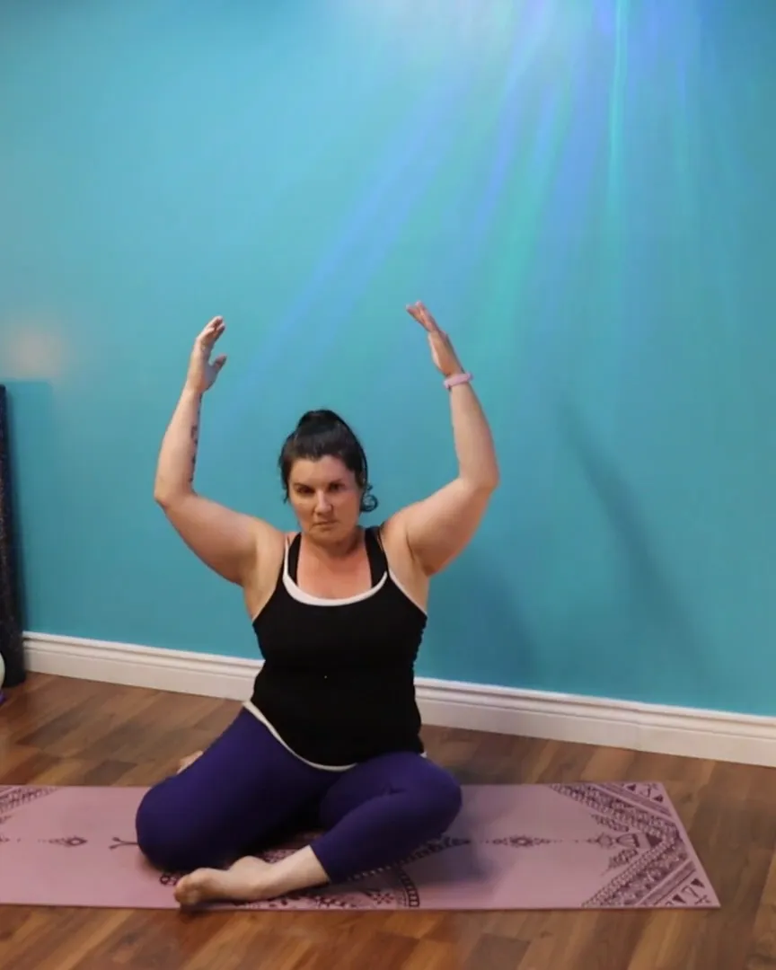 Angélique seated cross-legged with both arms raised