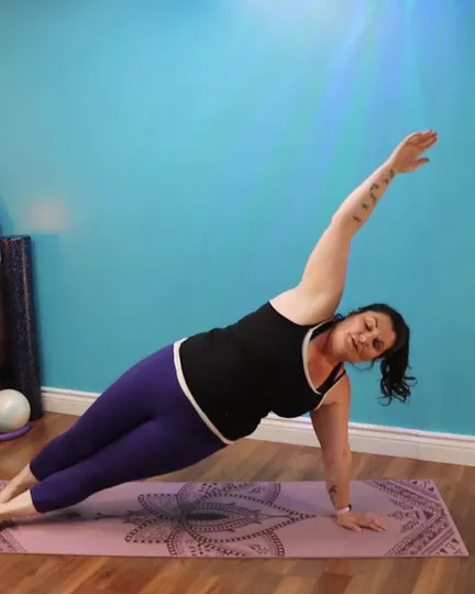 Angélique in a side plank on her mat, top arm reaching to the ceiling