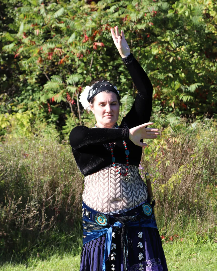 Angélique in her belly dance costume, one arm raised high, framed by autumn leaves