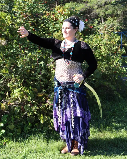 Angélique in her belly dance costume, reaching one arm out, a curved sword at her hip